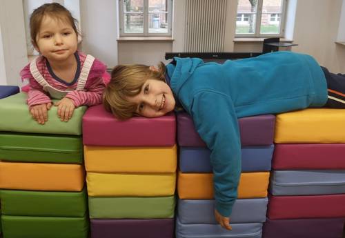 Zwei Kinder liegen auf einer bunten Mauer aus quadratischen Kissen