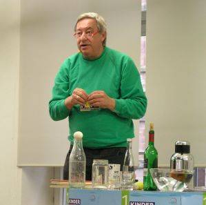 Christoph Biemann auf der Bühne bei seinem Besuch in der Stadtbibliothek Offenburg. Vor ihm stehen alle möglichen Utensilien für seine Exprimente.
